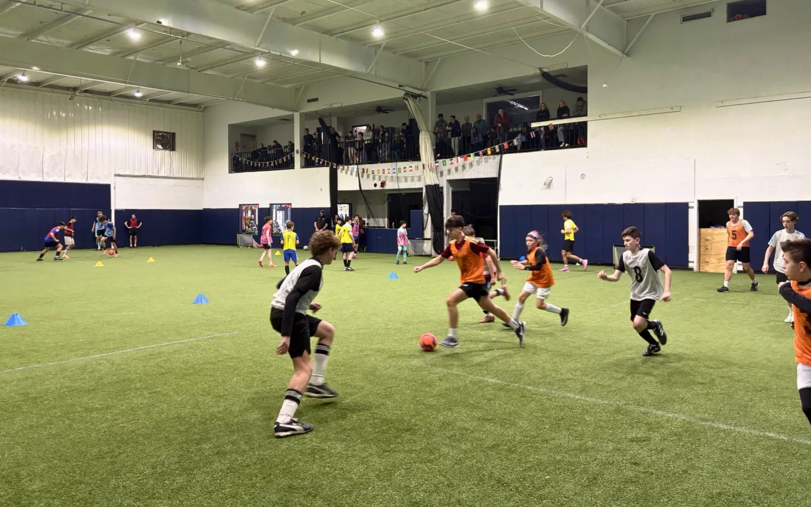 Kids in pinnies racing for the ball during an indoor turf soccer game at Bedford Field House.