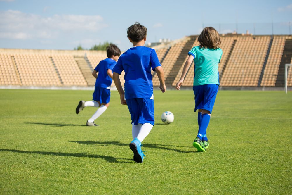 Youth athletes running a soccer skills drill on indoor turf with a coach.